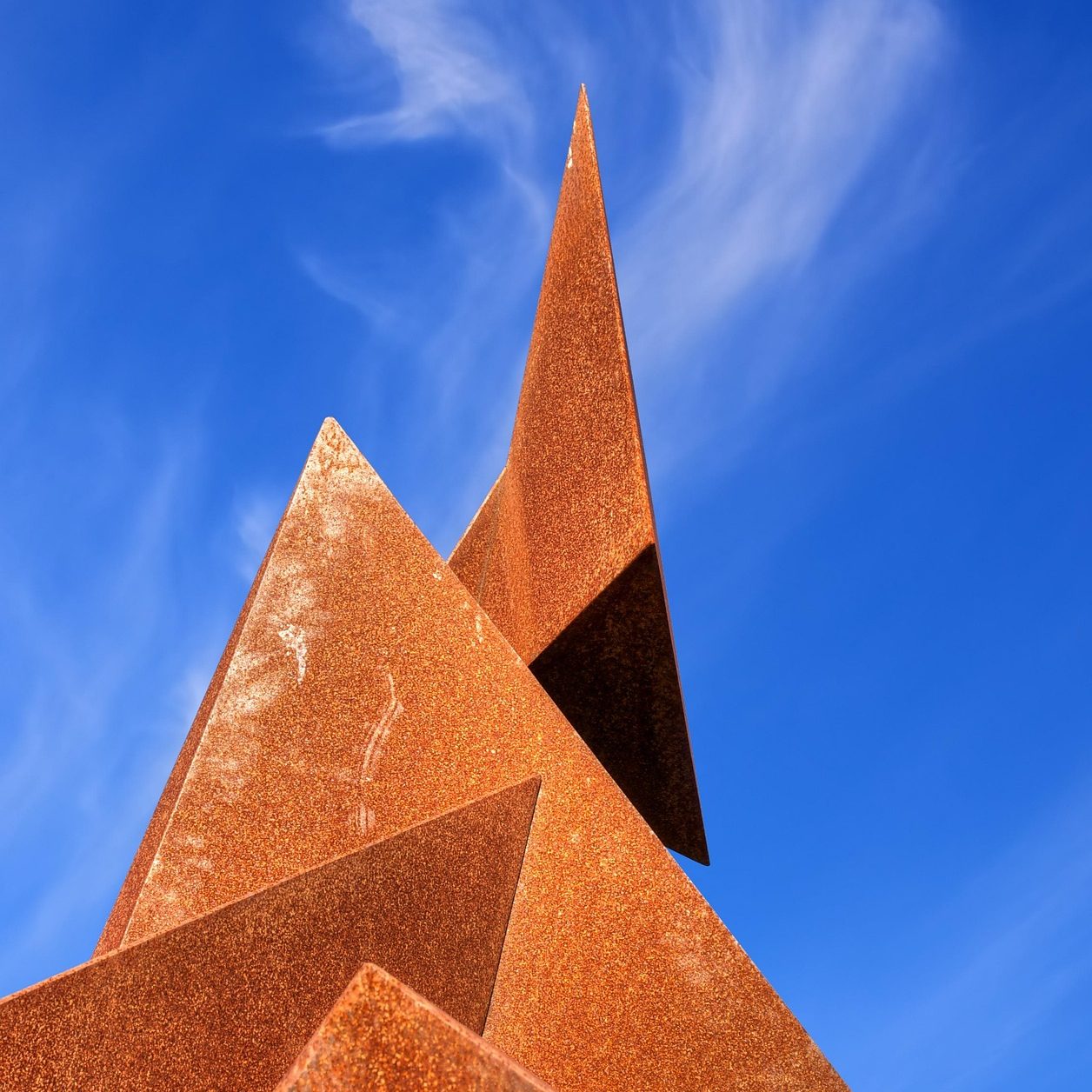 A rusted metallic structure made of pyramides and standing toward a blue sky.